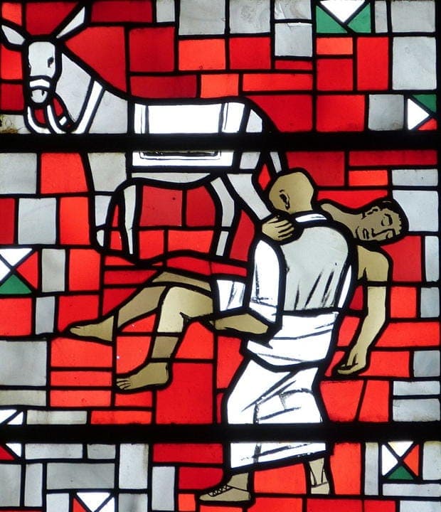 Stained glass art showing a man carrying another with a donkey nearby.